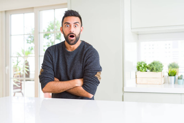Hombre hispano guapo vistiendo suéter casual en casa asustado y sorprendido con expresión sorpresa, miedo y cara excitada
. - Foto, imagen