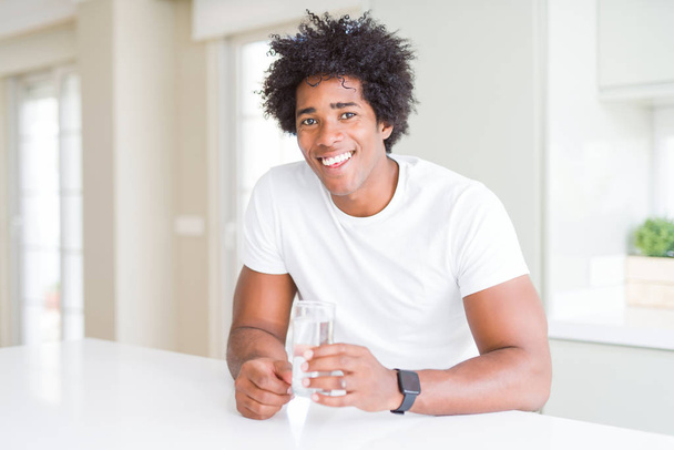 Hombre afroamericano bebiendo un vaso de agua en casa con una cara feliz de pie y sonriendo con una sonrisa confiada mostrando los dientes
 - Foto, imagen