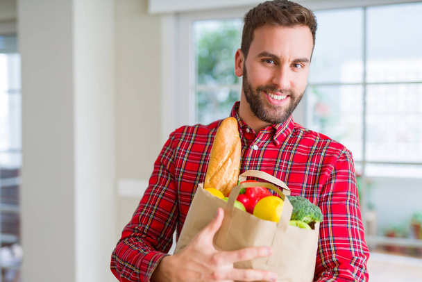 Handsome man holding paper bag full of fresh groceries at home - Foto, immagini