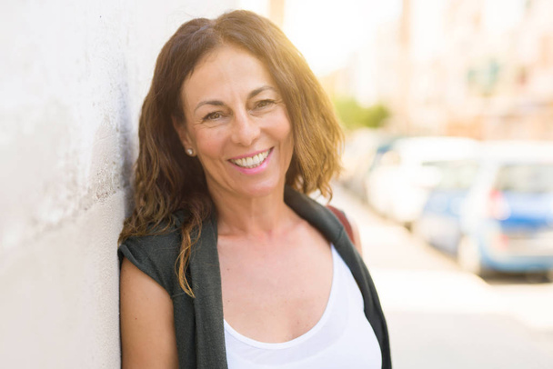 Beautiful middle age woman smiling cheerful leaning on a brick w - Photo, Image