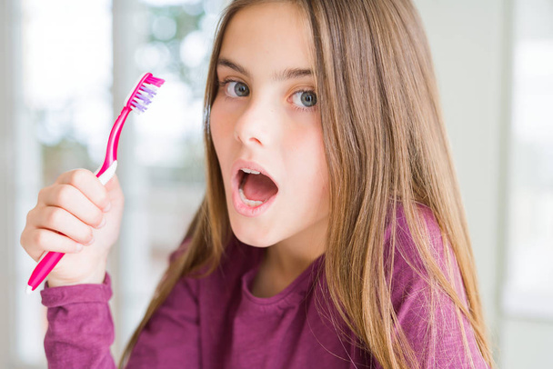 Красивая молодая девочка с розовой зубной щеткой, напуганная от шока с неожиданным лицом, напуганная и взволнованная выражением страха
 - Фото, изображение