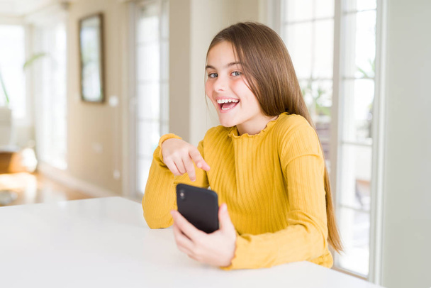 Menina bonita criança enviando uma mensagem usando smartphone muito feliz apontando com a mão e o dedo
 - Foto, Imagem