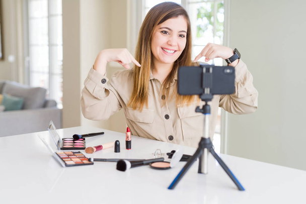 Beautiful young influencer woman recording make up video tutorial looking confident with smile on face, pointing oneself with fingers proud and happy. - Photo, Image