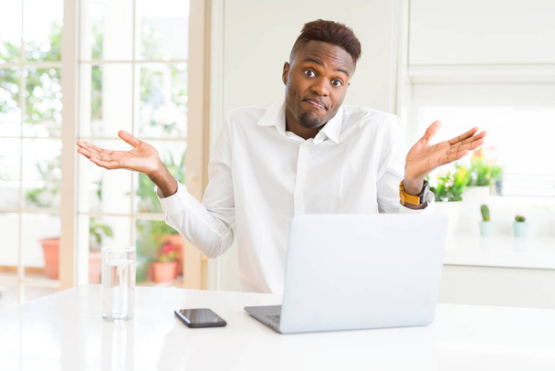 Afrikkalainen amerikkalainen liikemies työskentelee kannettavan tietokoneen tietämätön ja sekava ilme kädet ja kädet ylhäällä. Epävarma käsite
. - Valokuva, kuva