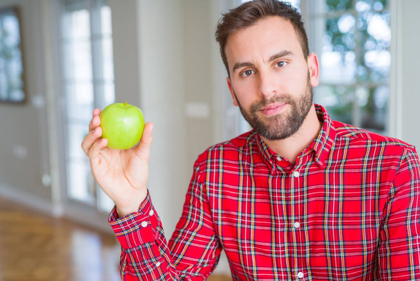 Szép ember eszik friss egészséges zöld alma, a Szúró Szembenéz gondolkodás súlyos magabiztos kifejezés - Fotó, kép