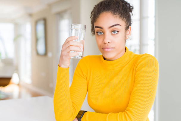 Jeune femme afro-américaine boire un verre d'eau douce avec une expression confiante sur la pensée intelligente visage grave
 - Photo, image