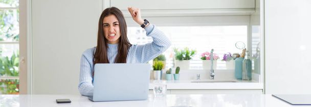 Широке зображення красивої молодої жінки, яка працює або вчиться за допомогою ноутбука роздратований і розчарований крик з гнівом, божевіллям і криком з піднятою рукою, концепцією гніву
 - Фото, зображення