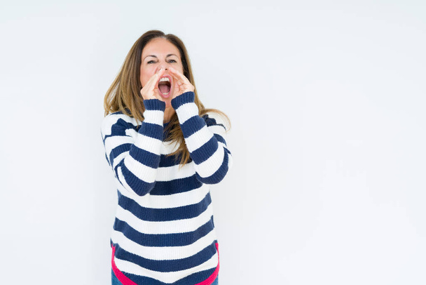 Красивая женщина средних лет в темно-синем свитере на изолированном фоне кричит громко, с руками над ртом
 - Фото, изображение
