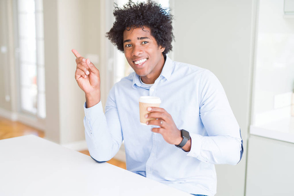 Hombre afroamericano con pelo afro bebiendo una taza de café para llevar muy feliz señalando con la mano y el dedo hacia un lado
 - Foto, Imagen
