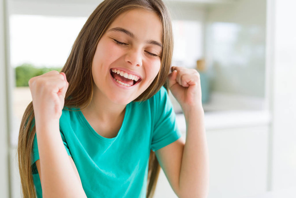 笑顔で勝利を祝って育った腕で成功に興奮した緑の t シャツを着た美しい若い女の子の子供。勝者コンセプト. - 写真・画像