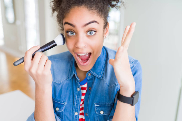 Young african american girl appying blush using make up brush very happy and excited, winner expression celebrating victory screaming with big smile and raised hands - Photo, Image