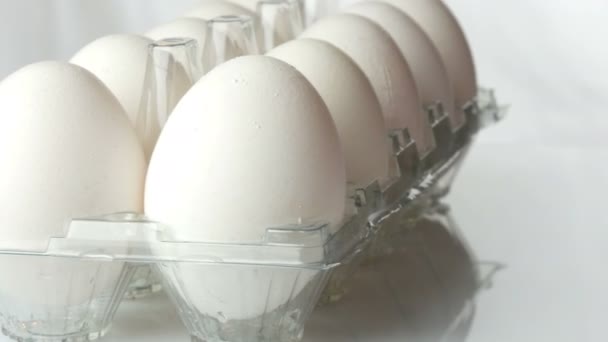 Huevos de pollo blancos grandes en bandeja de plástico transparente sobre un fondo blanco
 - Metraje, vídeo