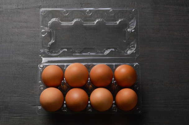 Siyah arka planda şeffaf plastik kutuda kahverengi yumurta - Fotoğraf, Görsel