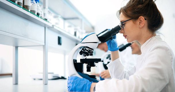 Young female scientist looking through microscope in laboratory - Φωτογραφία, εικόνα