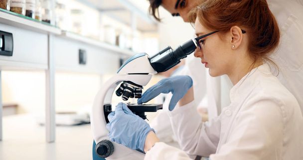 Young female scientist looking through microscope in laboratory - Photo, image
