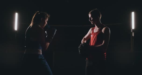 Hermosa boxeadora morena trabajando golpes en las patas con un entrenador en una habitación oscura
 - Imágenes, Vídeo