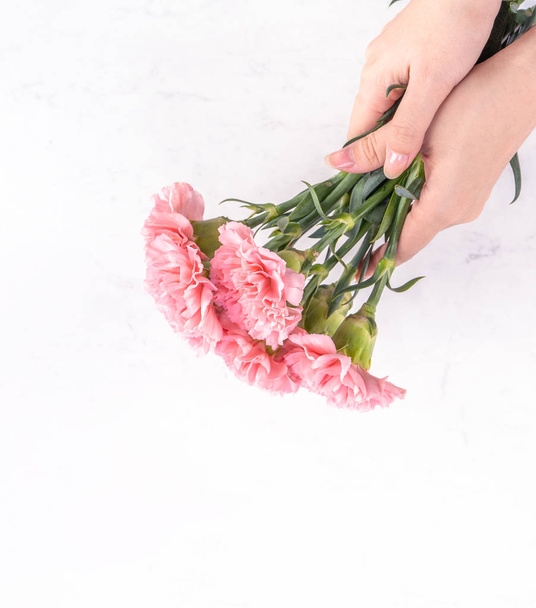 Woman giving bunch of elegance blooming baby pink color tender carnations isolated on bright marble background, mothers day decor design concept, top view, close up, copy space - Photo, Image