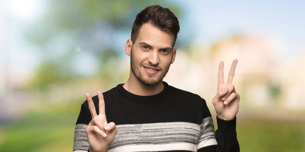 Handsome man smiling and showing victory sign with both hands at outdoors - Фото, зображення