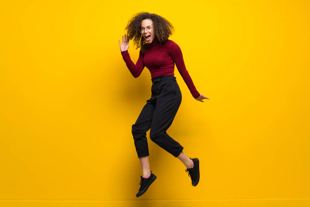Dominican woman with curly hair jumping over isolated yellow wall - Valokuva, kuva