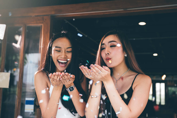 zwei asiatische Frauen blasen Papierkonfetti für eine Feier in seinem  - Foto, Bild