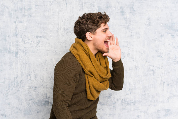 Homem loiro sobre a parede grunge gritando com a boca bem aberta para o lateral
 - Foto, Imagem