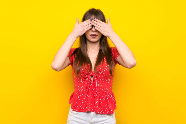 Mujer joven sobre pared amarilla cubriendo los ojos con las manos
 - Foto, imagen