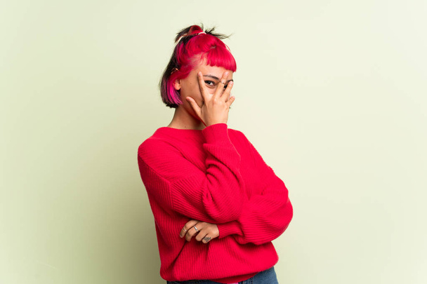 Young woman with red sweater covering eyes by hands and looking through the fingers - Photo, Image