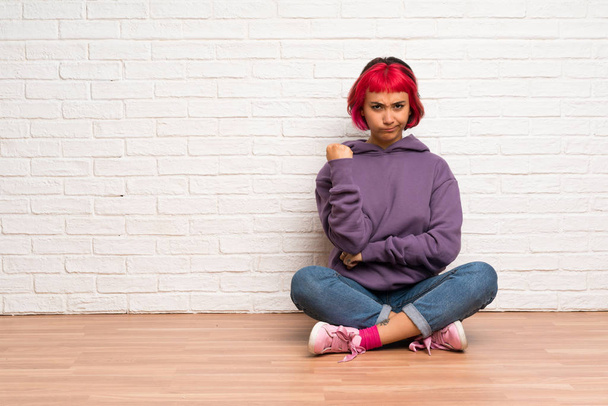 Νεαρή γυναίκα με ροζ μαλλιά που κάθεται στο πάτωμα με θυμωμένος χειρονομία - Φωτογραφία, εικόνα