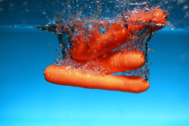 Carrot in the water splash over blue - 写真・画像