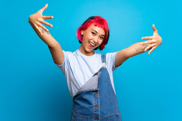 junge Frau mit rosa Haaren über blauer Wand, die mit den Fingern zehn zählt - Foto, Bild