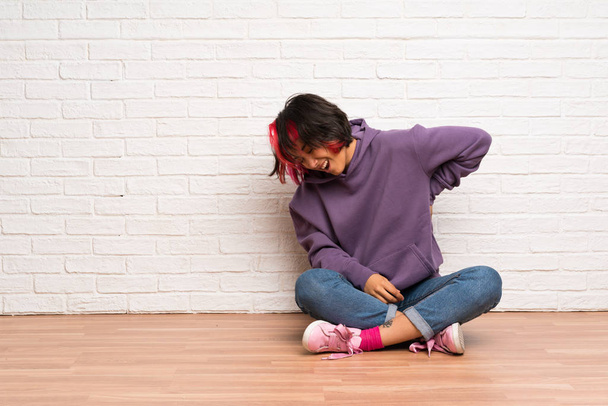 Νεαρή γυναίκα με ροζ μαλλιά που κάθεται στο πάτωμα που πάσχουν από οσφυαλγία για έχοντας κάνει μια προσπάθεια - Φωτογραφία, εικόνα