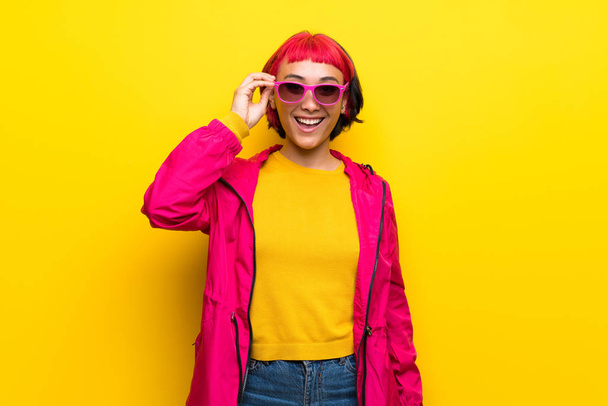 Young woman with pink hair over yellow wall with glasses and surprised - Фото, зображення