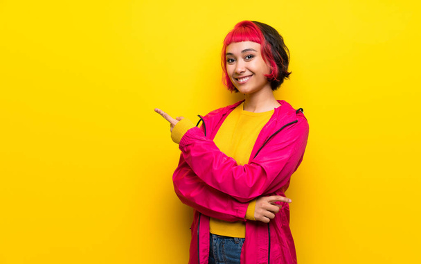 Jeune femme avec les cheveux roses sur le mur jaune pointant doigt sur le côté
 - Photo, image