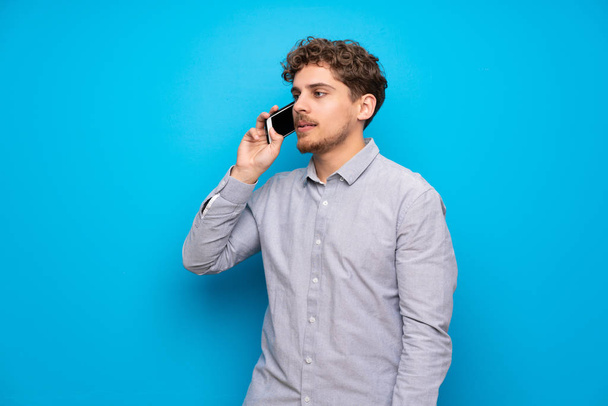 Szőke férfi kék falon, hogy a beszélgetés a mobiltelefon - Fotó, kép