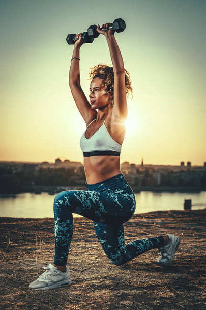 junge Fitness-Frau beim Workout mit Kurzhanteln vor Sonnenuntergang - Foto, Bild