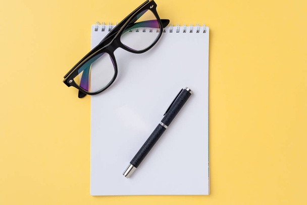 Notebook, eyeglasses and office stationery on bright yellow background - Fotoğraf, Görsel