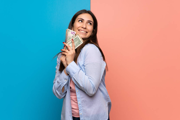 Young woman over pink and blue wall taking a lot of money - Фото, изображение