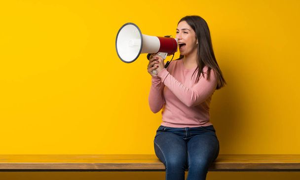Young woman sitting on table shouting through a megaphone - Foto, Bild