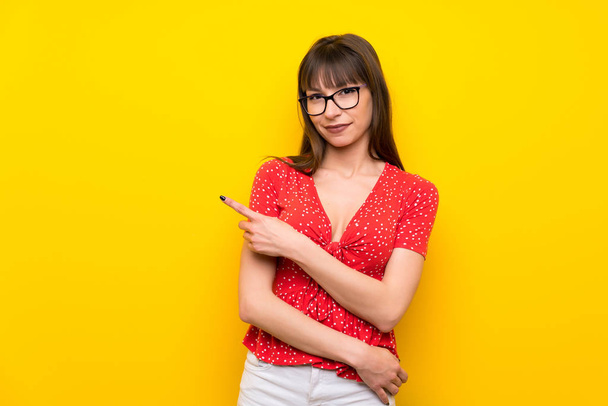 Fiatal nő oldalára mutató sárga falon bemutatni egy termék - Fotó, kép