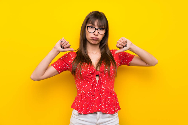 Jovem mulher sobre a parede amarela mostrando polegar para baixo
 - Foto, Imagem
