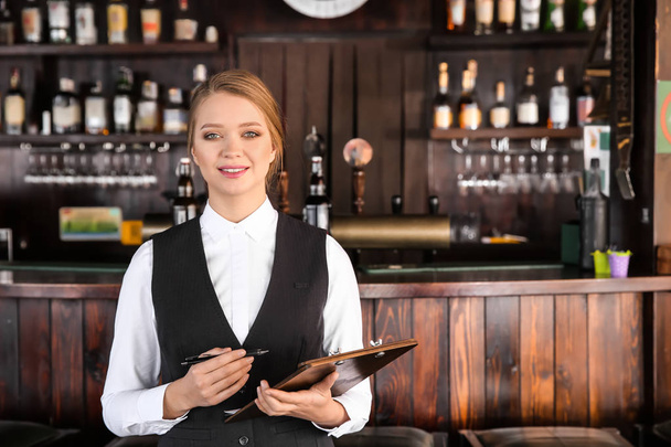 Young female waiter with clipboard in restaurant - Foto, afbeelding