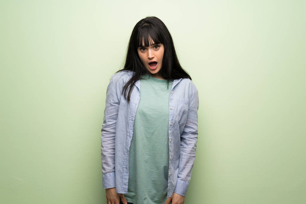 Young woman over green wall with surprise and shocked facial expression - Foto, Imagen