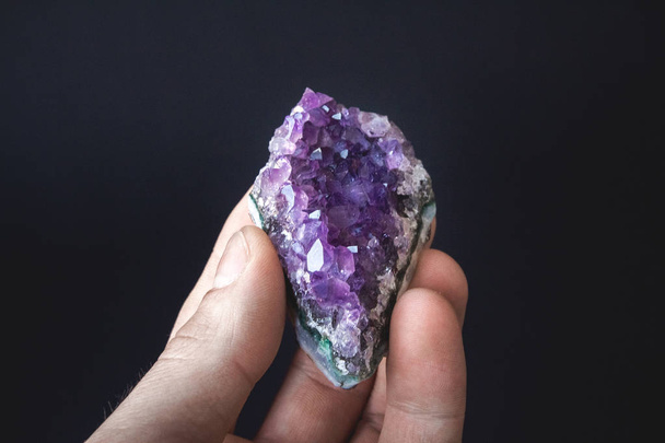 druse of natural untreated violet crystals of amethyst on a piece of rock lies on the palm of your hand - Fotoğraf, Görsel