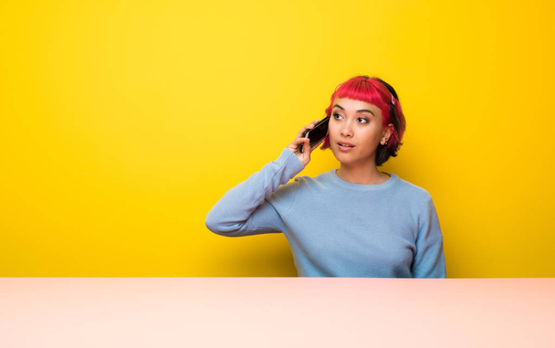 Nuori nainen vaaleanpunaiset hiukset pitää keskustelun matkapuhelimen kanssa
 - Valokuva, kuva