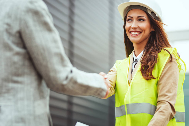 Nuori onnistunut naisinsinööri valkoisessa kypärässä kättelee manageria
 - Valokuva, kuva