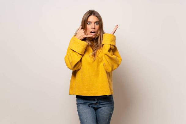 Woman with yellow sweater over isolated wall making phone gesture and doubting - Foto, imagen