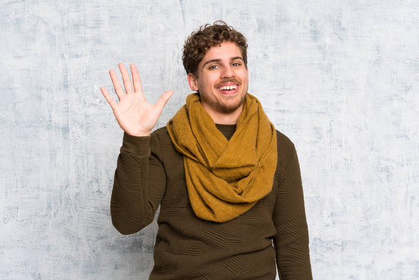Hombre rubio sobre la pared grunge saludando con la mano con expresión feliz
 - Foto, Imagen