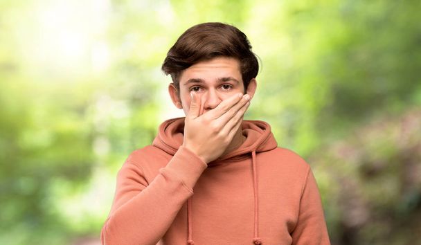 Hombre adolescente con sudadera cubriendo la boca con las manos por decir algo inapropiado al aire libre
 - Foto, Imagen