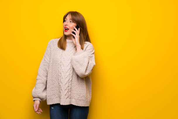 rothaarige Frau über gelbe Wand, die ein Gespräch mit dem Handy führt - Foto, Bild
