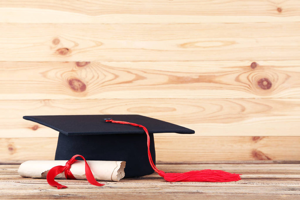 Graduation cap with diploma on brown wooden table - Fotó, kép